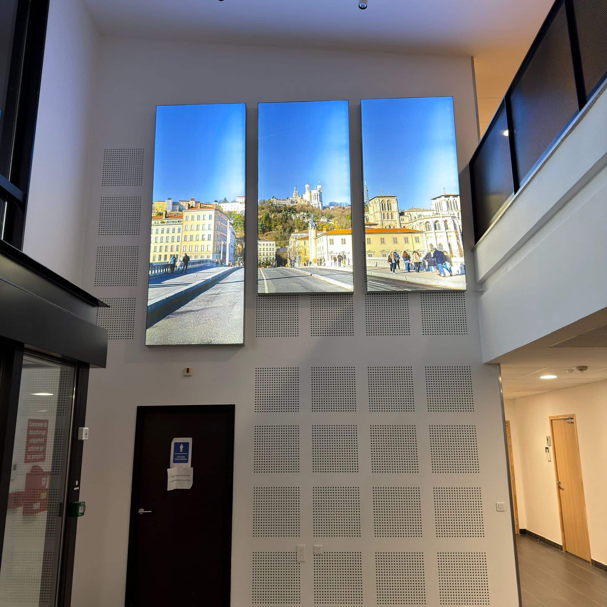 Trois grands panneaux lumineux verticaux affichant des vues de Lyon dans le hall d'entrée d'un bâtiment