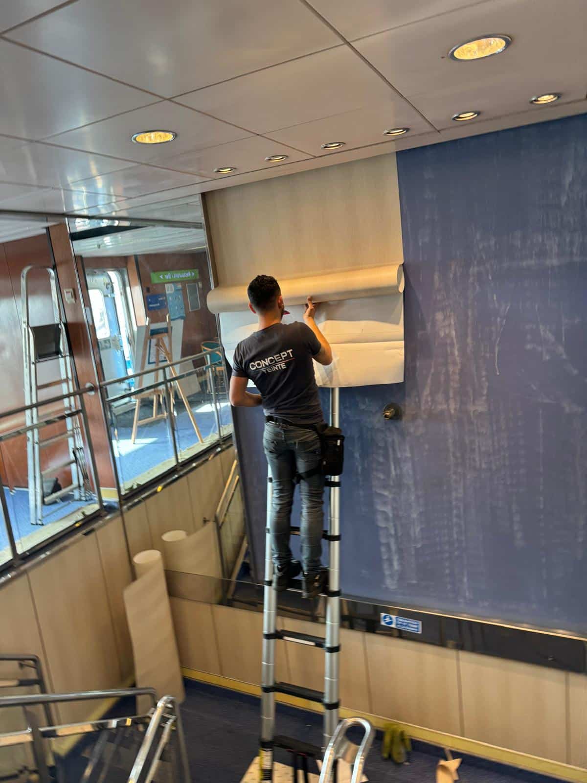 Technicien Concept Teinte sur une échelle posant un revêtement adhésif effet bois clair sur d'anciens panneaux muraux bleus