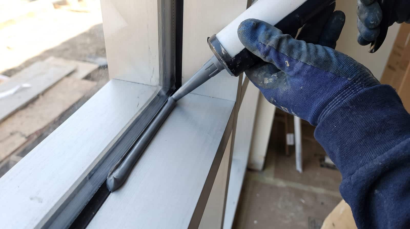 Détail d'un cordon de mastic d'ancrage entre un film de sécurité et le cadre d'une fenêtre