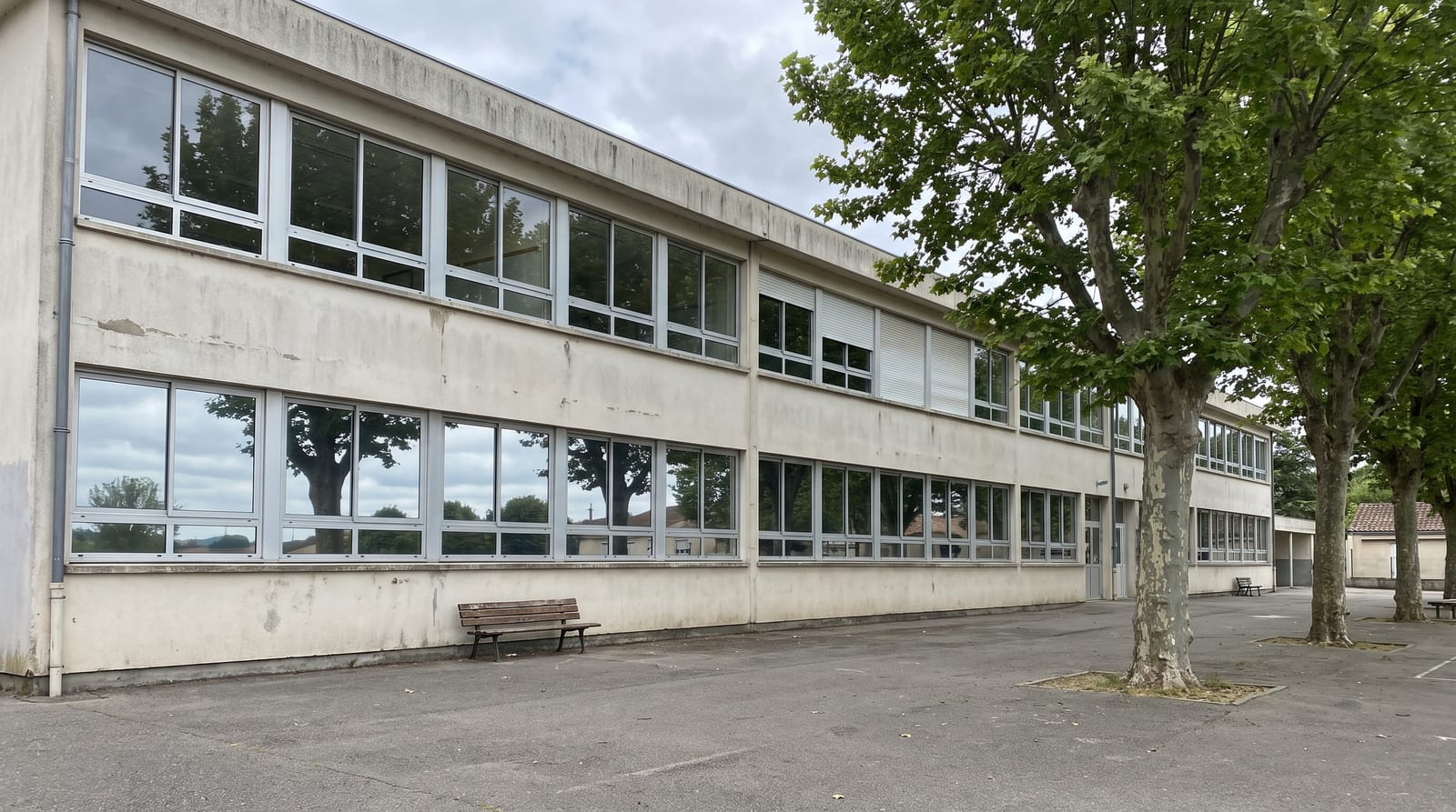 Façade d'école aux fenêtres de rez-de-chaussée équipées d'un film réfléchissant, cour vide