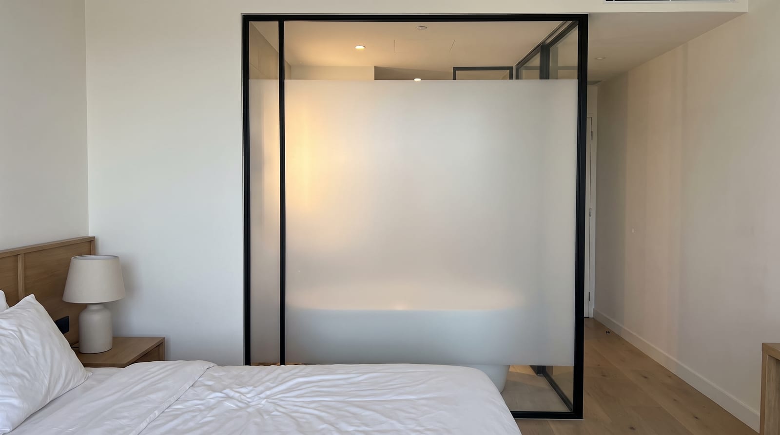 Salle de bains d'hôtel séparée de la chambre par une paroi vitrée rendue opaque par un film